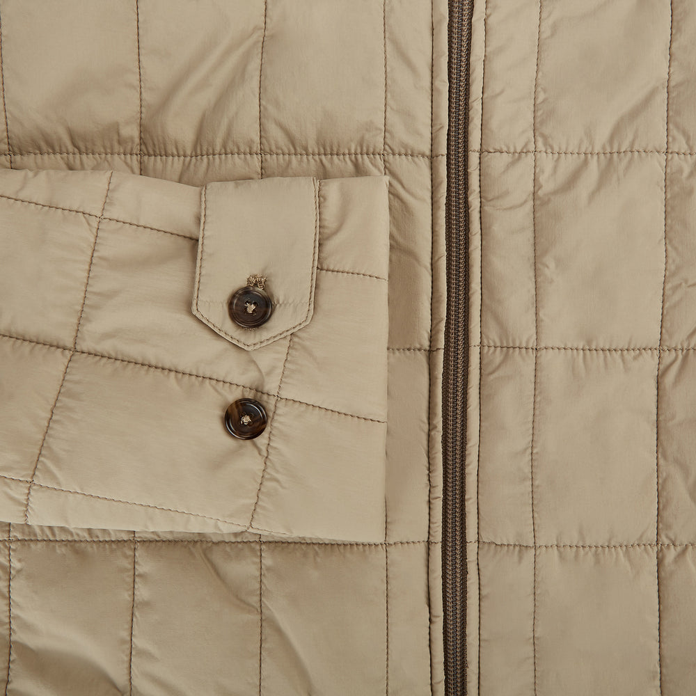 The Battersea Sand Quilted Jacket by Turnbull & Asser is a light beige men's jacket with a front zipper, pointed collar, zippered side pockets, chest pocket, and buttoned cuffs, shown on a plain white background.