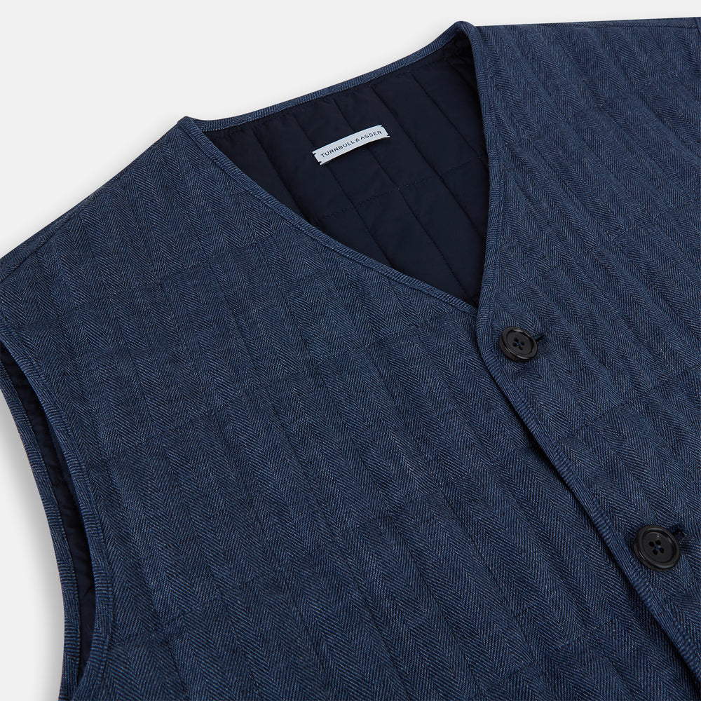 The Denim Blue Quilted Linen Herringbone Waistcoat by Turnbull & Asser features a sleeveless design, five black buttons, two zippered side pockets, and a small chest pocket against a plain white background.