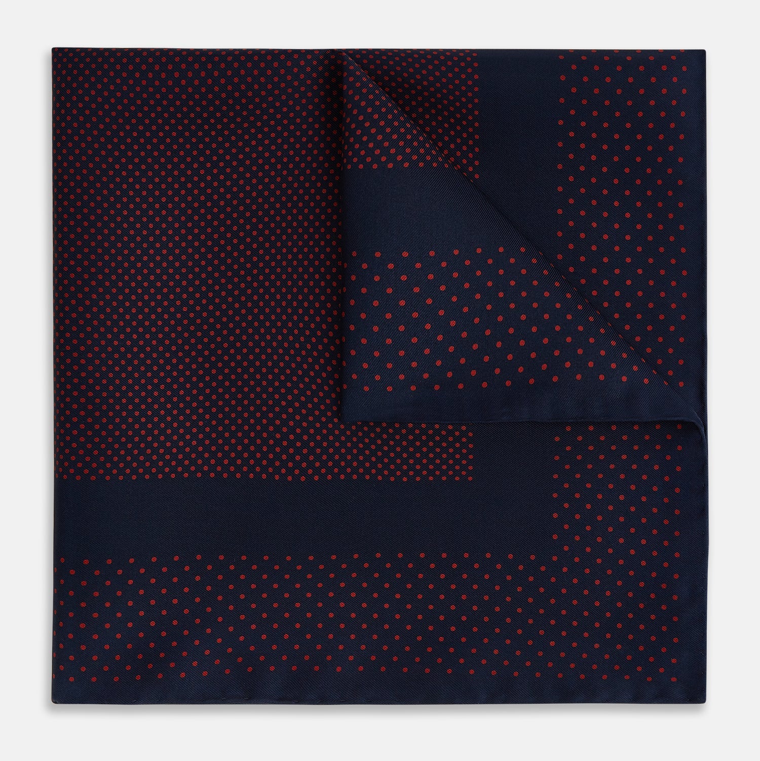 View 1 of product The Turnbull & Asser Navy and Red Dot Silk Pocket Square features a dark navy blue base with small red polka dots on the border and inner pattern, all handmade and neatly folded.