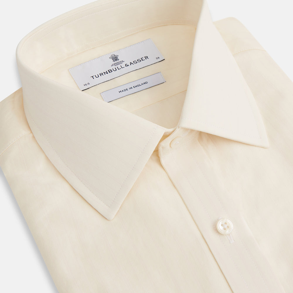 The Cream Fine Pencil Stripe Mayfair Shirt by Turnbull & Asser features long sleeves, a pointed collar, and buttoned cuffs. Crafted from breathable cotton with fine pencil stripes, it is shown laid flat on a white background.