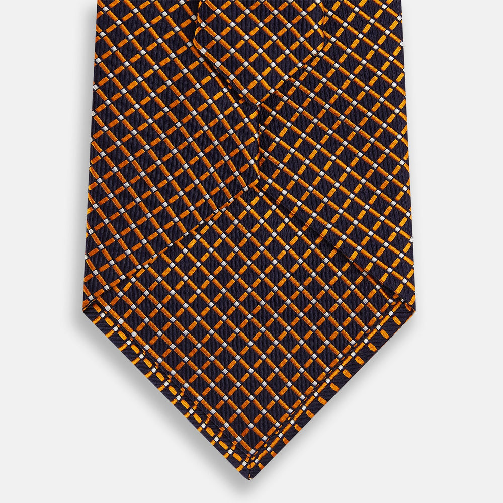 The Turnbull & Asser Orange and Navy Diamond Silk Tie features a yellow and orange diamond pattern on navy silk, ideal for modern office attire, and is displayed rolled up on a light surface.