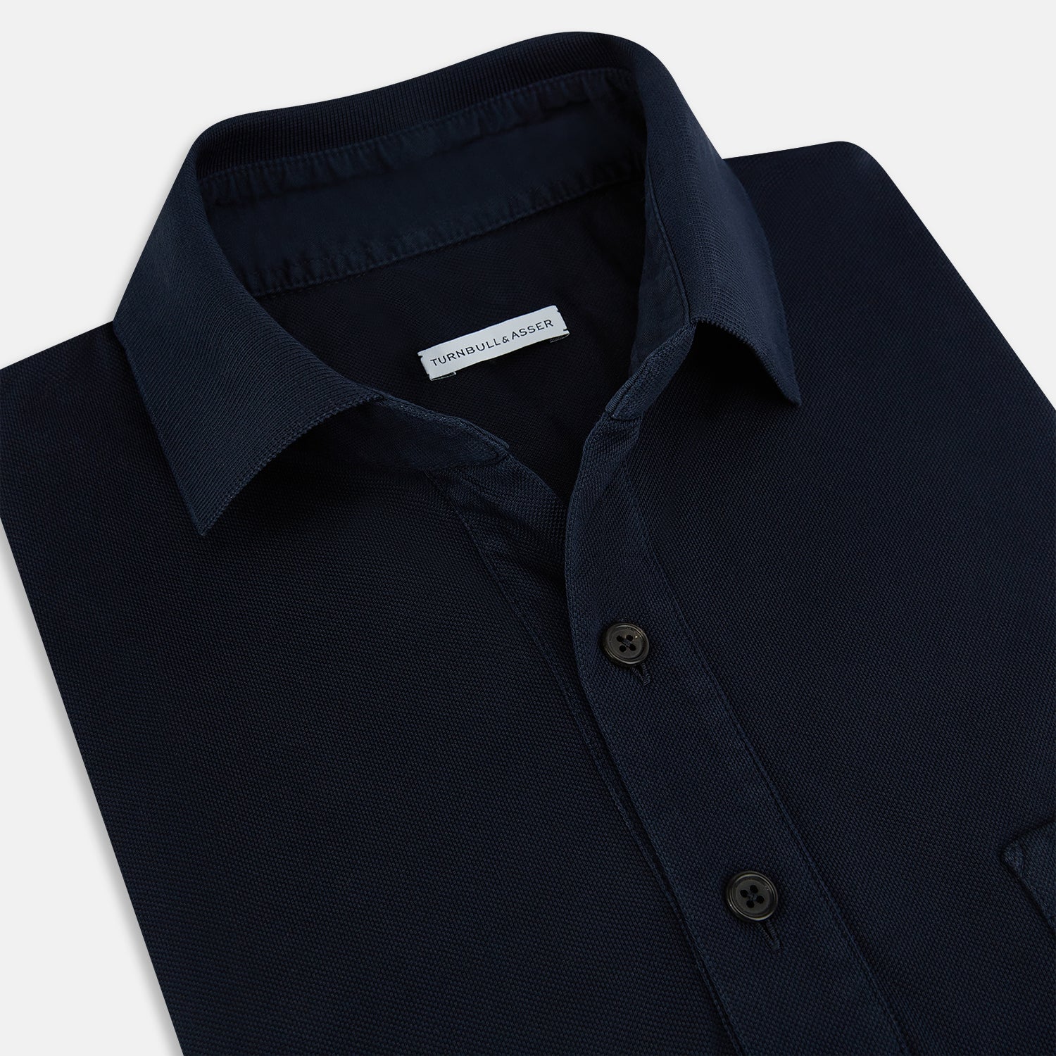 View 2 of product The Turnbull & Asser Navy Polo Shirt features short sleeves, a collar, three-button placket, and a single buttoned chest pocket, shown flat on a plain white background.
