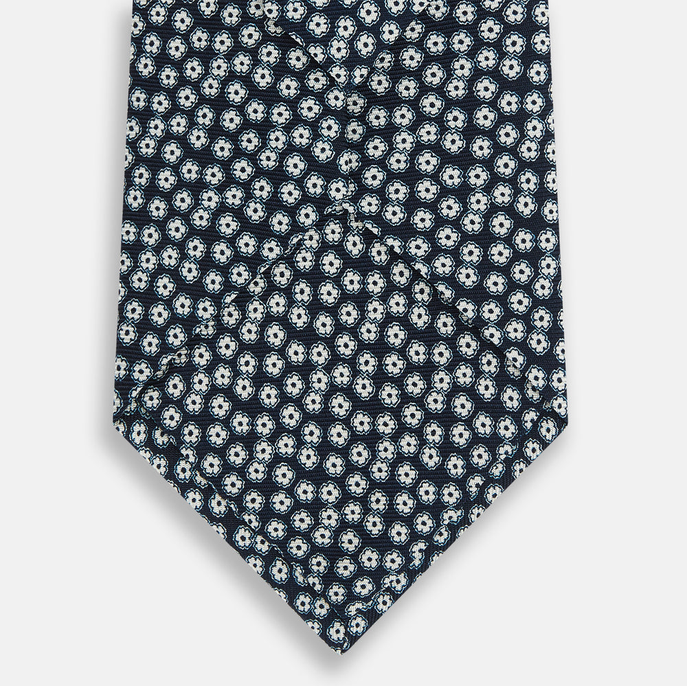 The Turnbull & Asser Navy Flower Patterned Printed Silk Tie features a repeating design of small white and light blue floral motifs on navy silk.