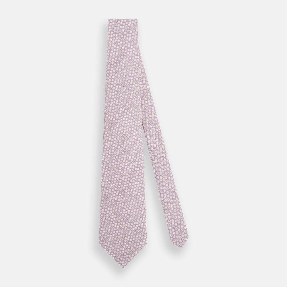 The Turnbull & Asser Lilac Flower-Patterned Printed Silk Tie, featuring a light lilac hue and small white circular designs, is shown rolled up against a plain white background.
