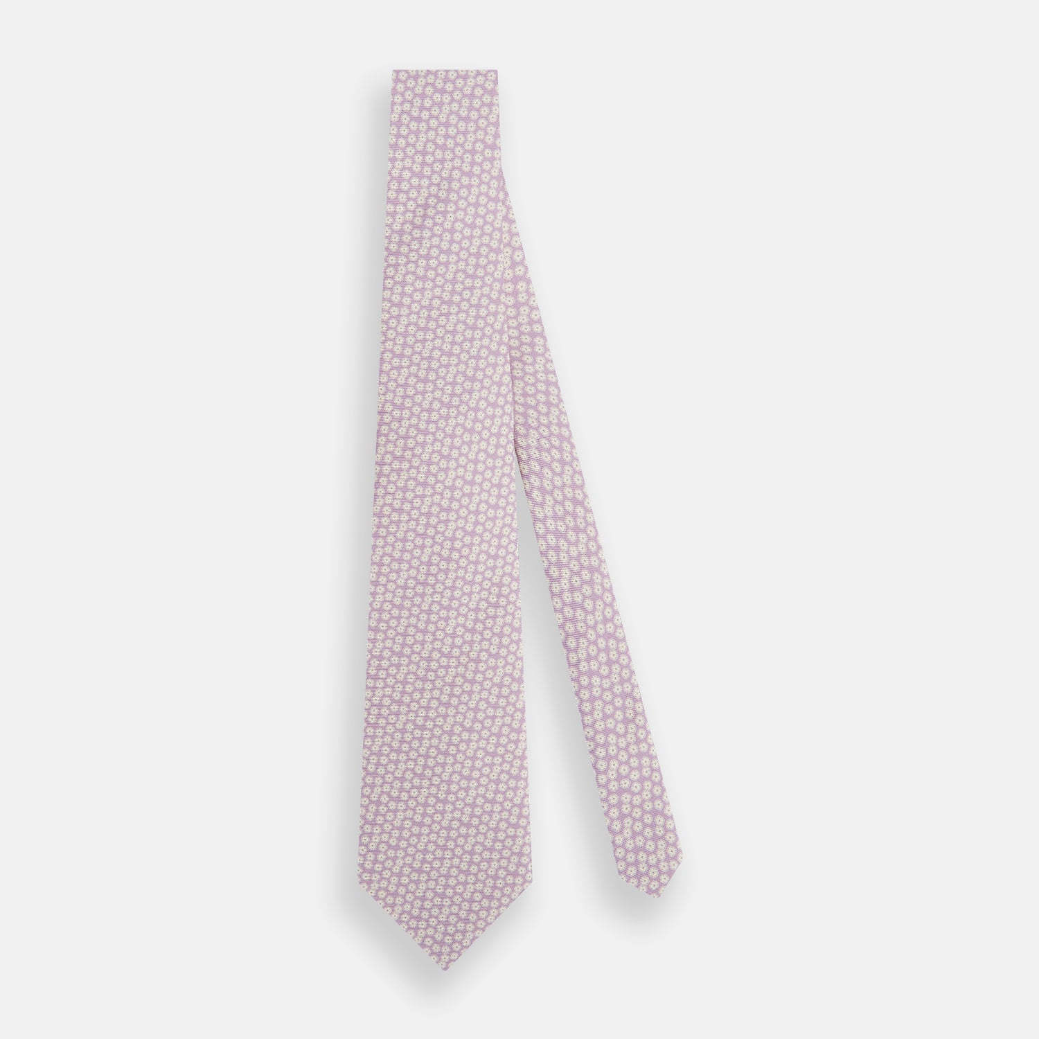 View 2 of product The Turnbull & Asser Lilac Flower-Patterned Printed Silk Tie, featuring a light lilac hue and small white circular designs, is shown rolled up against a plain white background.