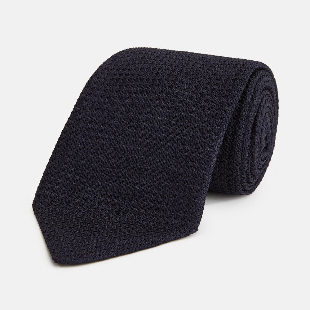 The GRENADINE NAVY TIE by Turnbull & Asser—a rolled, dark navy blue textured tie—serves as an essential accessory for smart outfits, shown against a plain white background.