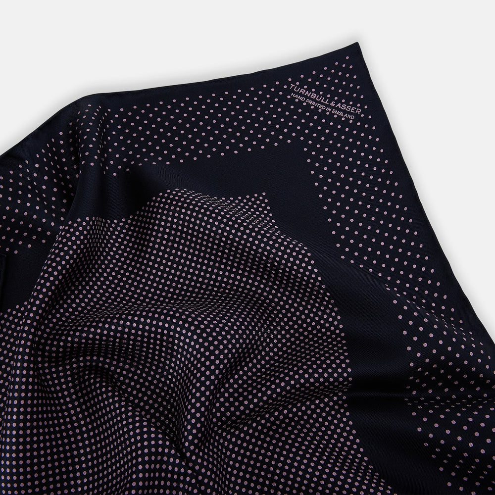 The Turnbull & Asser Navy and Lilac Dot Silk Pocket Square features small white polka dots with a wider border of spaced-out dots, neatly folded to showcase both sides of its handmade silk fabric.