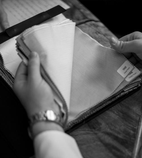 A person’s hands hold and flip through a fabric swatch book, examining different fabric samples on a table. The image is in black and white.