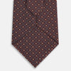 View 3 of product The Turnbull & Asser Burgundy Geometric Silk Tie, crafted in Britain, features a repeating pattern of light blue and white squares and diamonds. The neatly rolled tie is shown against a plain white background.