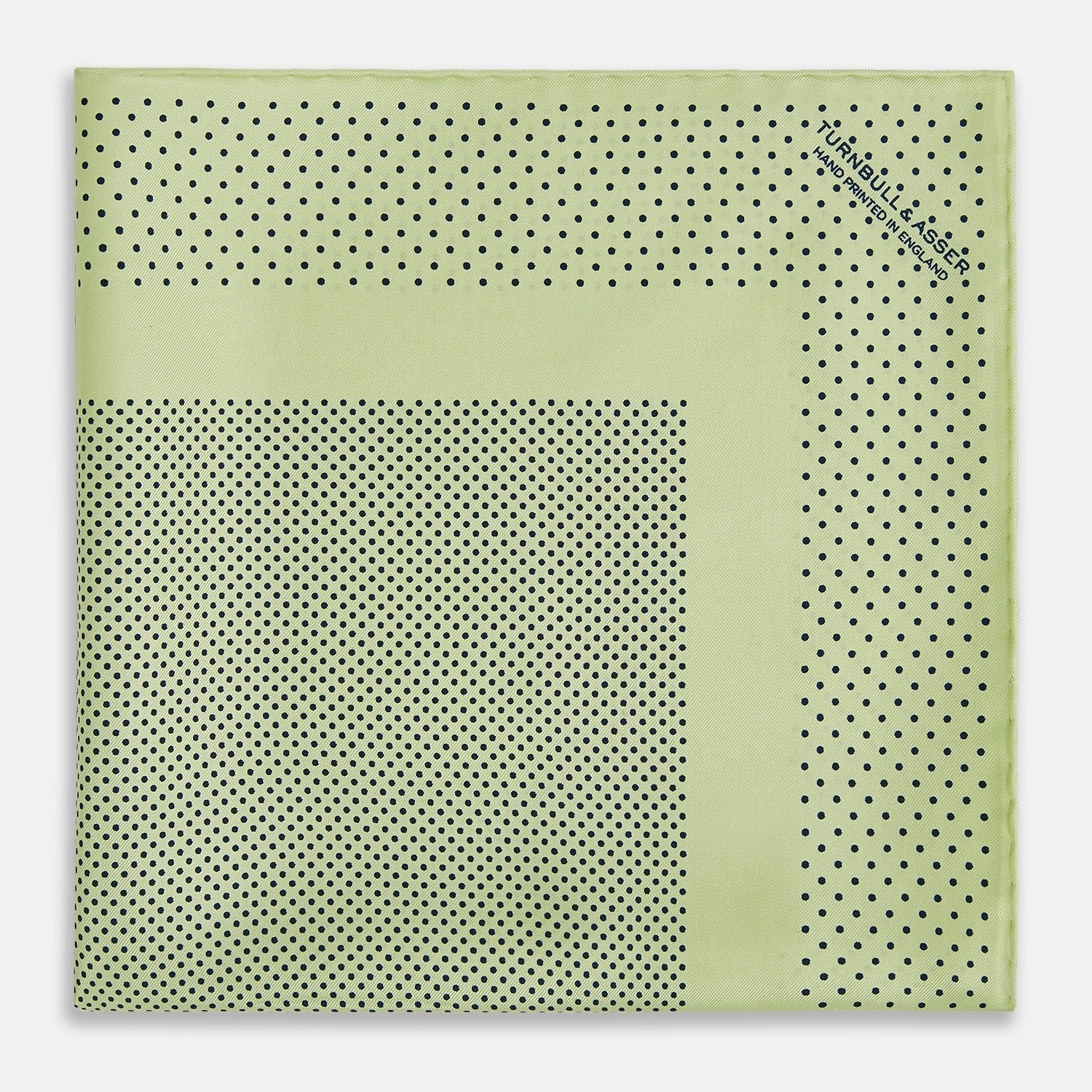 View 3 of product The Melon Green Dot Silk Pocket Square by Turnbull & Asser is handmade in England from silk, featuring small black polka dots. Shown folded with a turned-up corner, it displays both sides of the light green fabric.