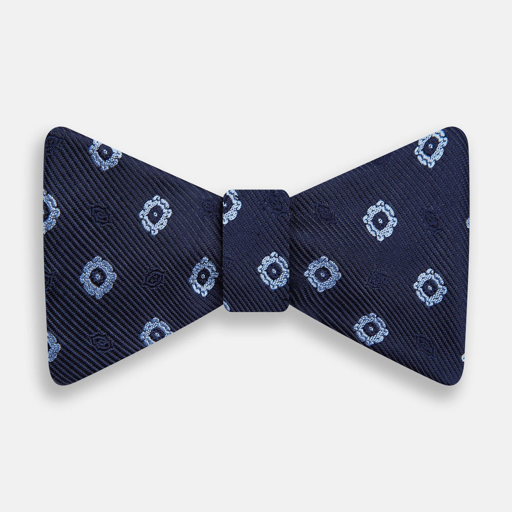 The Navy and Sky Blue Motif Silk Bow Tie by Turnbull & Asser features a subtle ribbed texture and light blue and white geometric floral patterns—an elegant choice for formalwear.