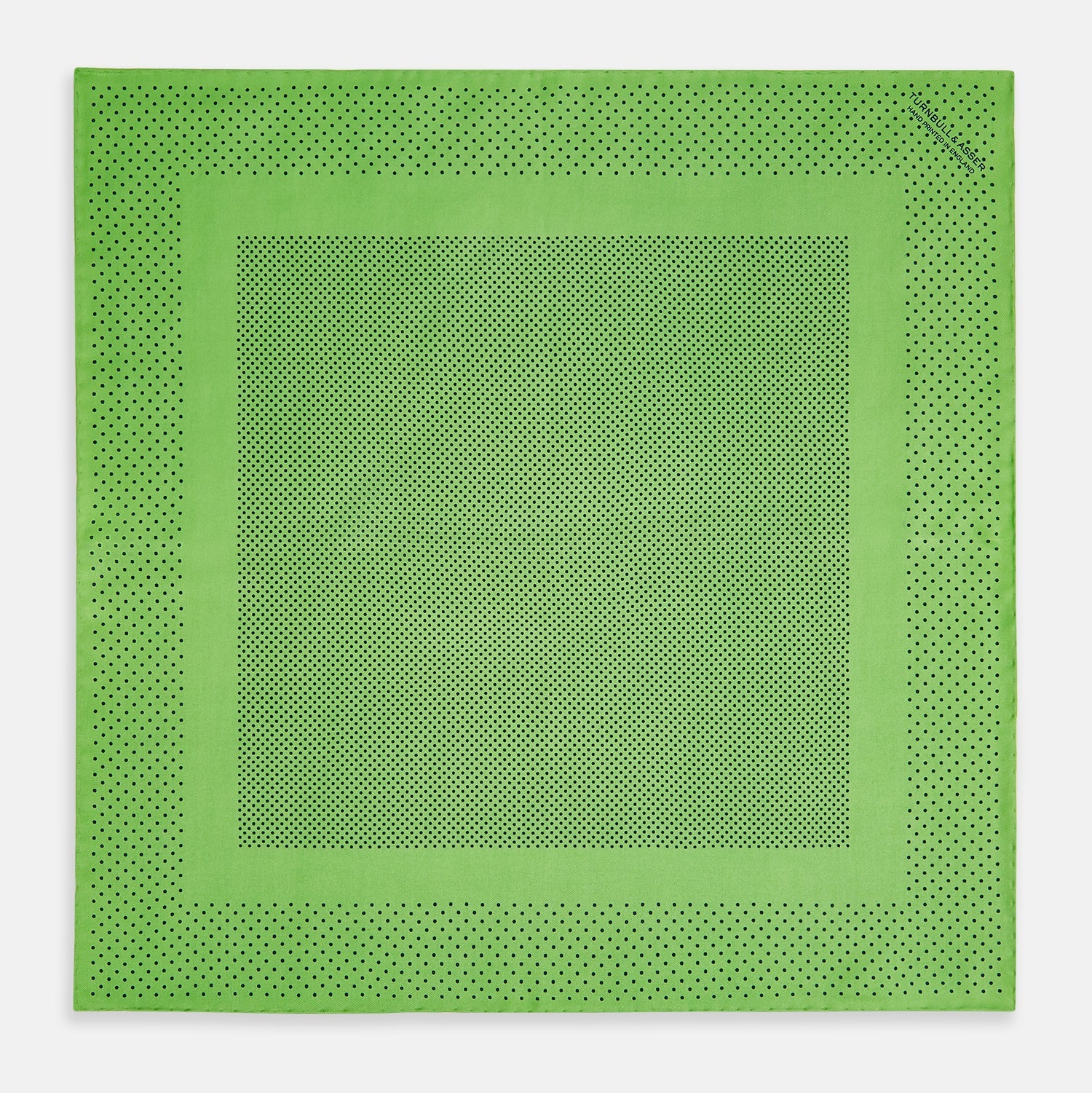 View 4 of product The Fern Green Dot Silk Pocket Square by Turnbull & Asser is crafted from pure silk, featuring a subtle black polka dot border with a denser dot pattern at the center and the brand name printed in the upper right corner.