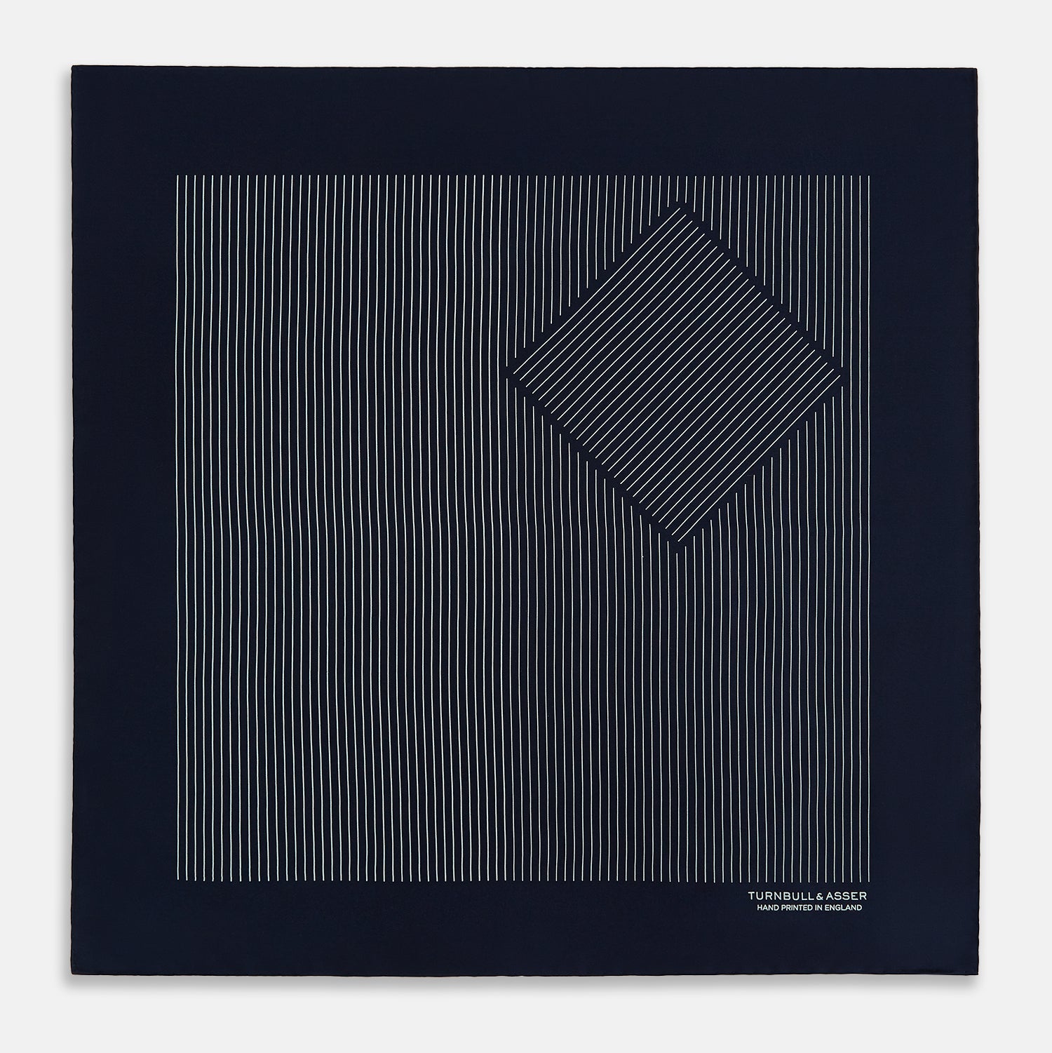 View 3 of product The Navy and White Stripe Silk Pocket Square by Turnbull & Asser features thin white vertical stripes and "TURNBULL & ASSER HAND PRINTED IN ENGLAND" in one corner, with a folded edge showing the reverse of this elegant silk accessory.