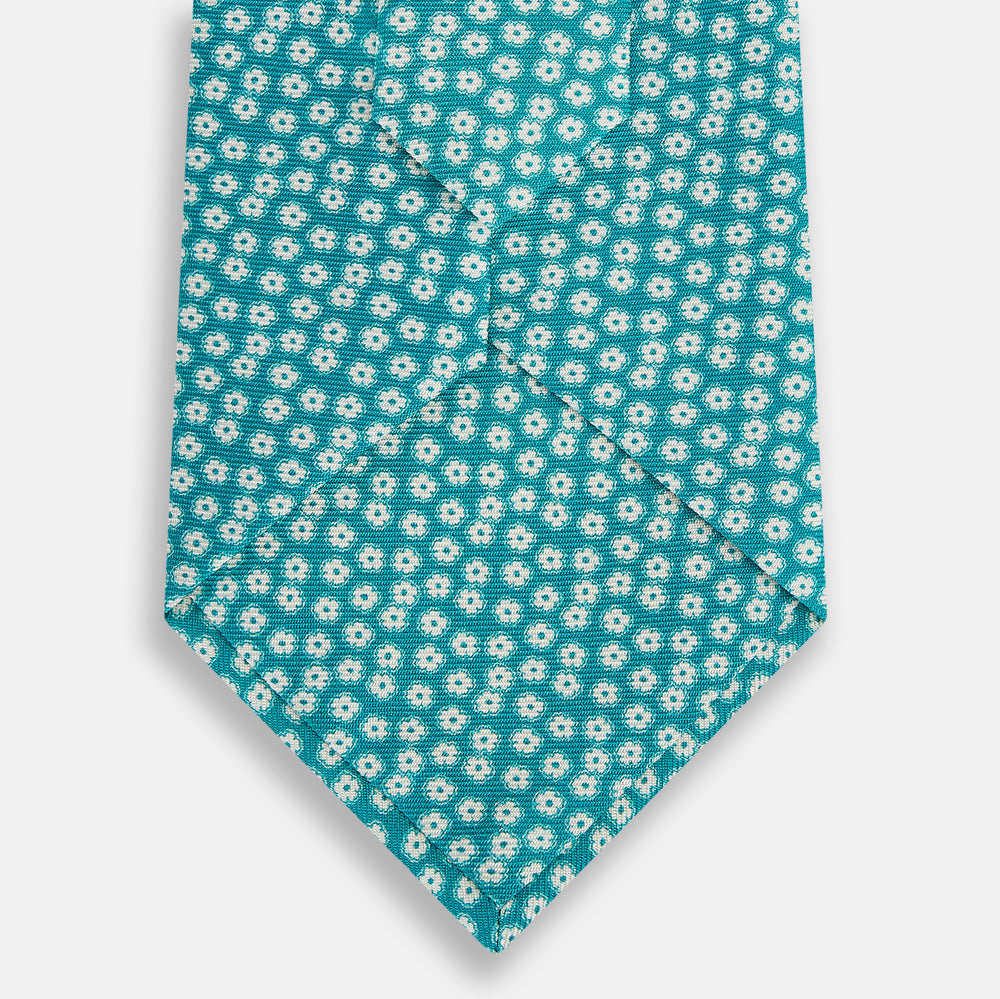 The Turnbull & Asser Turquoise Flower Patterned Printed Silk Tie, crafted from fine English silk, is neatly rolled on a white background.