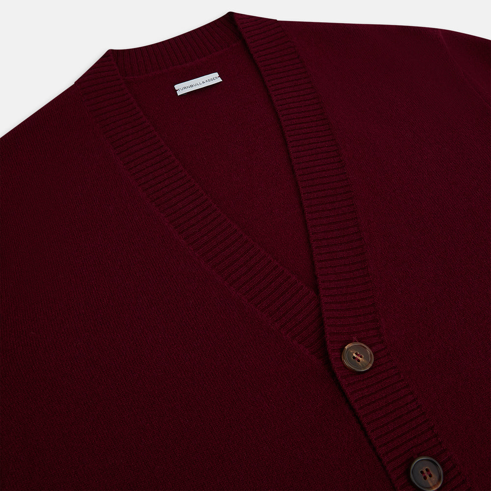 The Turnbull & Asser Burgundy Cashmere Cardigan features a V-neck, ribbed cuffs and hem, two front pockets, and a classic button-up design, shown on a plain white background.
