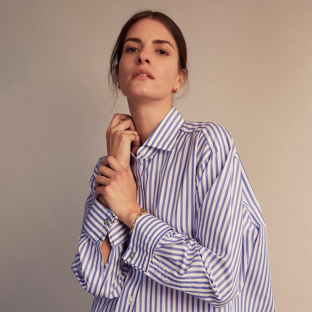 The Turnbull & Asser Pale Blue Candy Stripe Cotton Marlene Shirt is an oversized women's collared shirt with long sleeves, buttoned cuffs, and vertical blue and white stripes, shown laid flat on a white background.