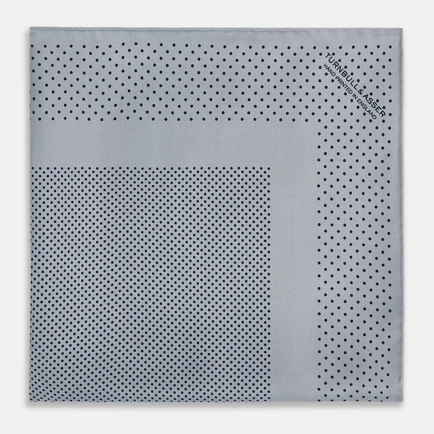 View 3 of product The Turnbull & Asser Grey Dot Silk Pocket Square features a light gray silk design with navy polka dots and a solid border. Elegantly handmade, it is shown with one corner folded to display both sides.