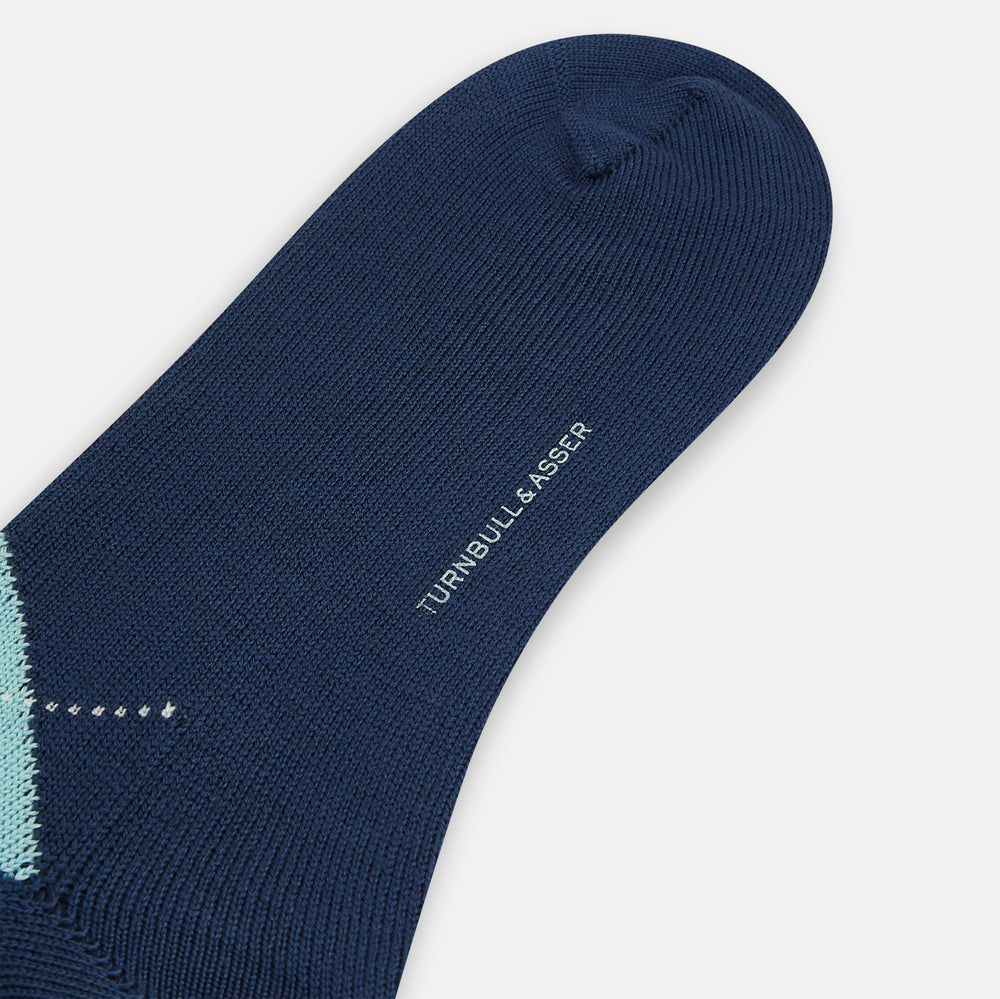 The Azzurro Wool Check Mid-Length Socks by Turnbull & Asser are navy blue with a ribbed cuff, featuring an argyle pattern in light blue, teal, and navy with white accents. Displayed upright against a plain white background.