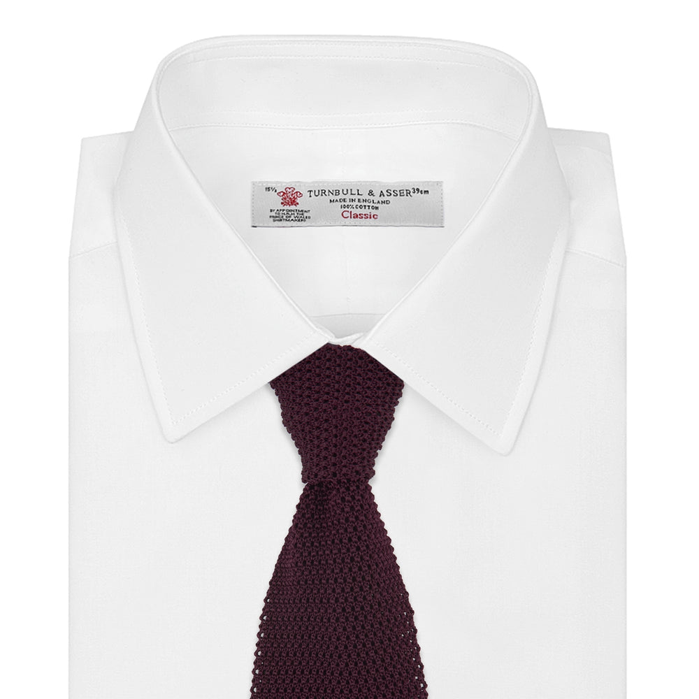 The Turnbull & Asser MTIE011-ZAI003 TIES 7.5CM is a plain burgundy tie shown rolled on a white background, featuring straight edges and textured knit—ideal for the modern gentleman’s versatile wardrobe.