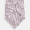 View 3 of product The Turnbull & Asser Lilac Flower-Patterned Printed Silk Tie, featuring a light lilac hue and small white circular designs, is shown rolled up against a plain white background.