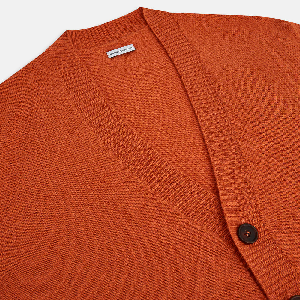The Orange Cashmere Cardigan by Turnbull & Asser showcases vibrant burnt orange, a V-neck, dark buttons, ribbed cuffs and hem, long sleeves, and two front pockets. Part of the knitwear collection; displayed on a white background.