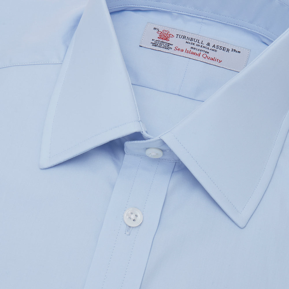 The Turnbull & Asser Light Blue Sea Island Quality Cotton Shirt features a T&A collar, double cuffs, white buttons, and a quality label inside the collar. Displayed on a plain white background.