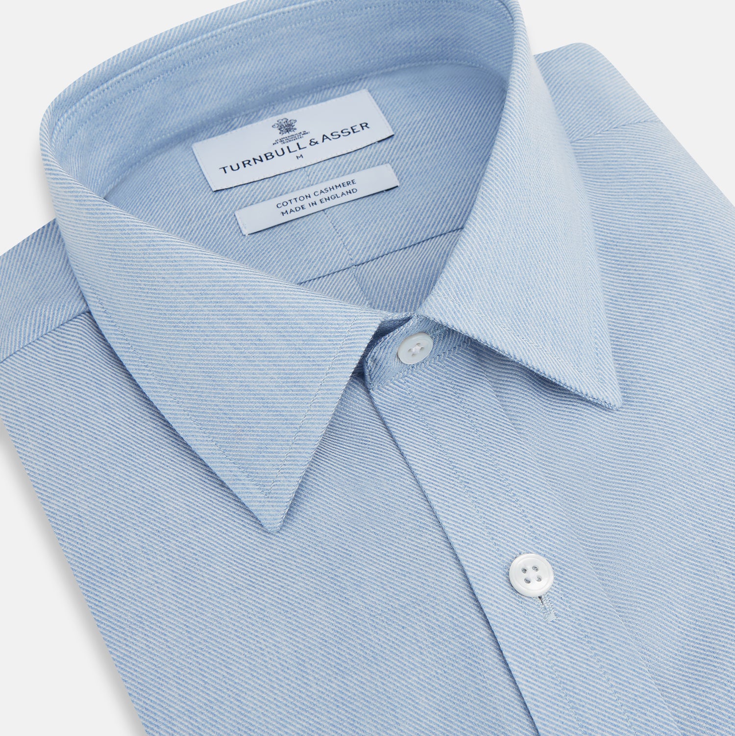 View 2 of product The Turnbull & Asser Pale Blue Cotton Cashmere Derby Collar Richmond Shirt features a soft cotton-cashmere blend, derby collar, white buttons, left chest pocket, and buttoned cuffs, shown laid flat on a white background.