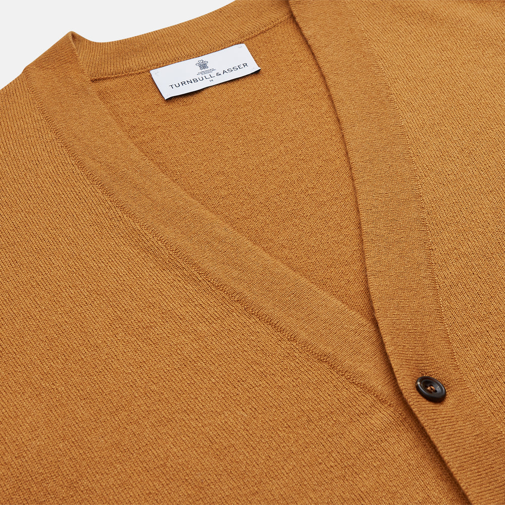 The Turnbull & Asser Golden Brown Cashmere Lachlan Cardigan features long sleeves, front buttons, two front pockets, and ribbed cuffs and hem—a luxurious knitwear piece shown laid flat on a white background.