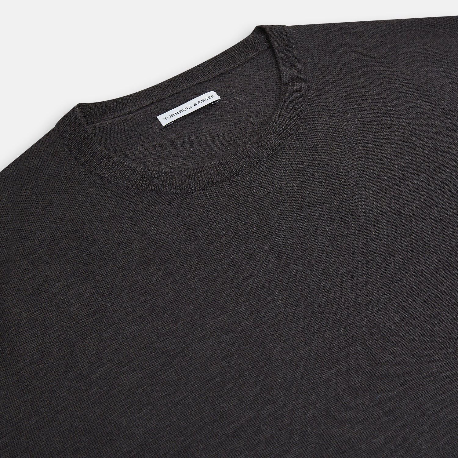View 2 of product The Turnbull & Asser Charcoal Grey Fine Merino Round Neck Jumper for men features long sleeves, ribbed cuffs, hem, and collar. Displayed on a white background, this classic knitwear piece has a plain design with no visible logos or patterns.