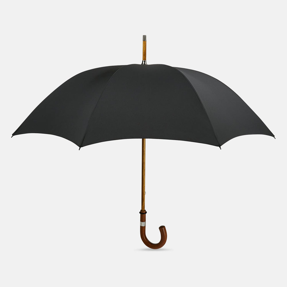 The Turnbull & Asser Black Traveller Umbrella features a Malacca crook handle and straight wooden shaft—a timeless accessory displayed fully opened against a white background.