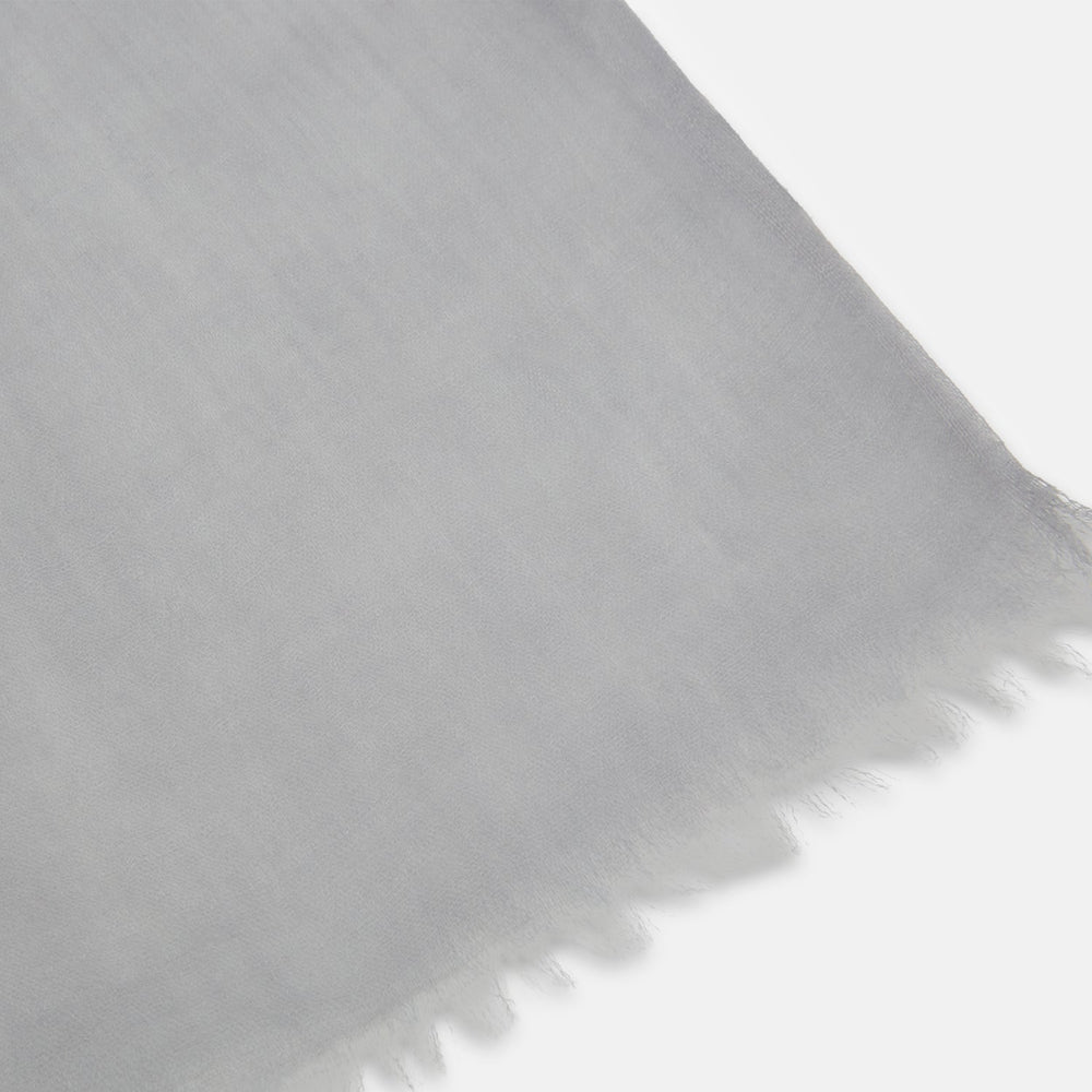 The Grey Cashmere Scarf by Turnbull & Asser, displayed folded with a loose knot on a white background, showcases semi-sheer luxury in light gray—an elegant accessory.