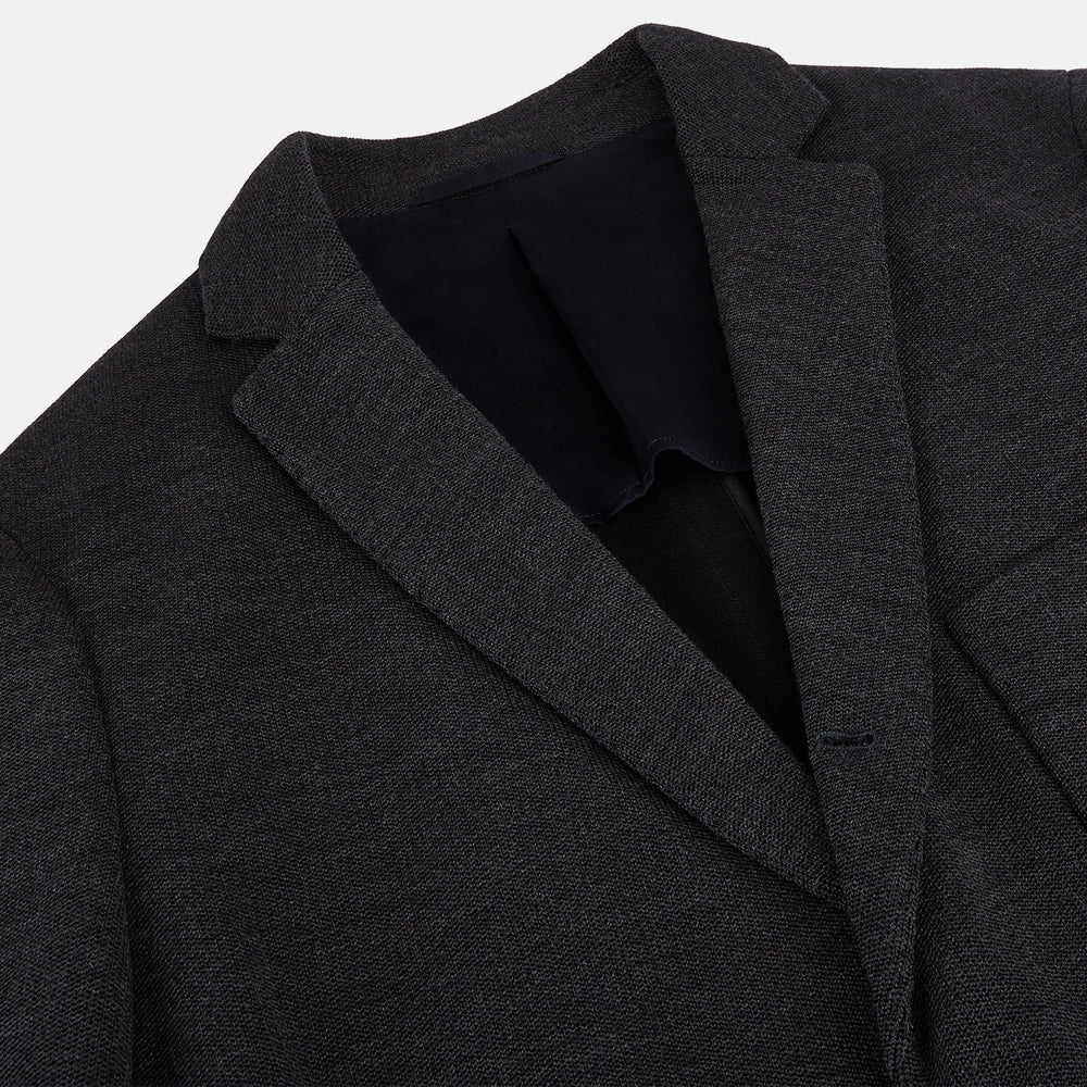 The Turnbull & Asser Charcoal Knitted Oxford Blazer features a notched lapel, two-button closure, and three front pockets, blending modern elegance with British heritage against a plain white background.