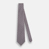 View 2 of product The Turnbull & Asser Ash Medallion Silk Tie is shown rolled up on a white background. This purple tie features a repeating geometric motif with small white circles and grid-like designs.