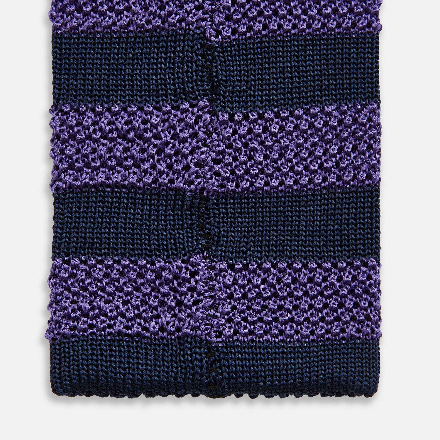 View 4 of product The KNITTED STRIPE PURPLE TIE by Turnbull & Asser features bold dark blue and purple stripes, making it an essential smart accessory. Shown rolled up on a white background.