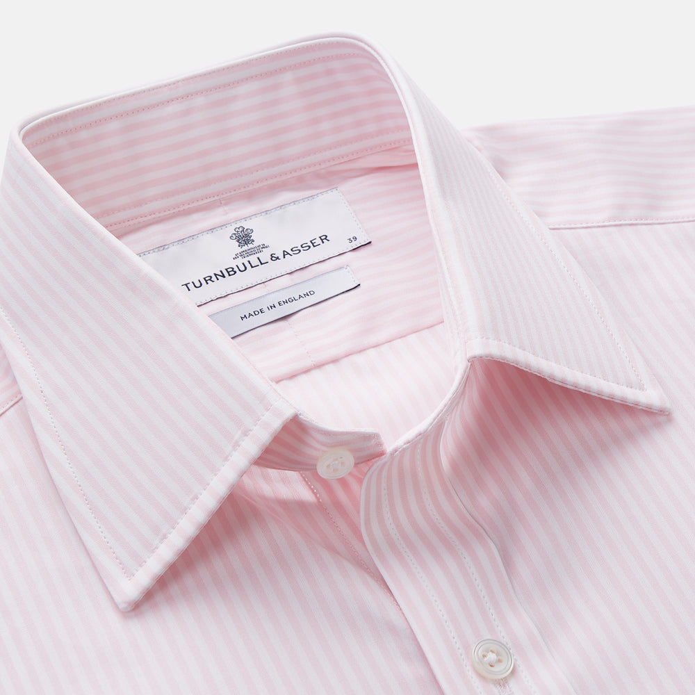 The Turnbull & Asser White and Pink Wide Stripe Mayfair Shirt features long sleeves, a collar, and bold vertical stripes, shown laid flat on a white background.