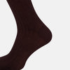 View 4 of product The Turnbull & Asser Oxblood Long Socks—a single, dark brown over-the-calf sock with a ribbed texture—are shown angled left on a plain white background, highlighting their length and fitted shape.