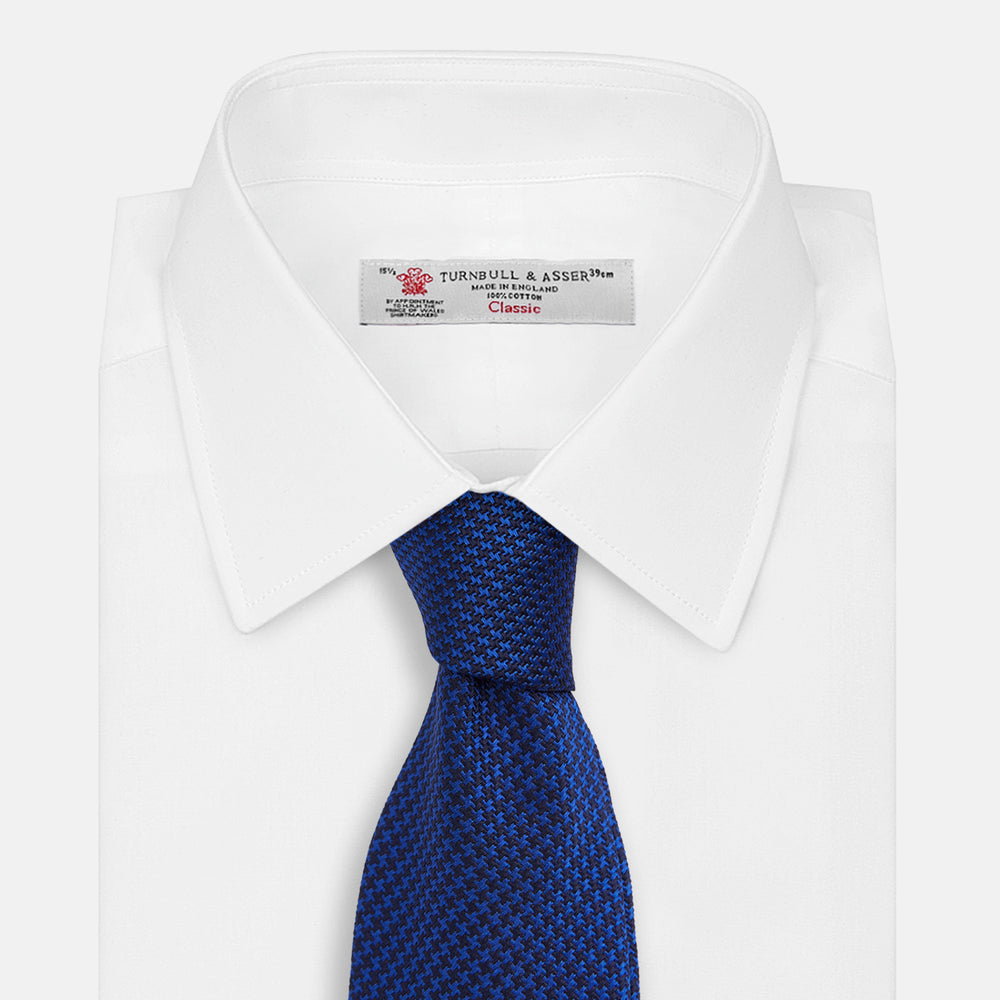 The HOUNDSTOOTH NAVY CRUISE TIE by Turnbull & Asser, featuring a textured blue design, is displayed rolled-up on a plain white background—an essential accessory for elevating formal looks.