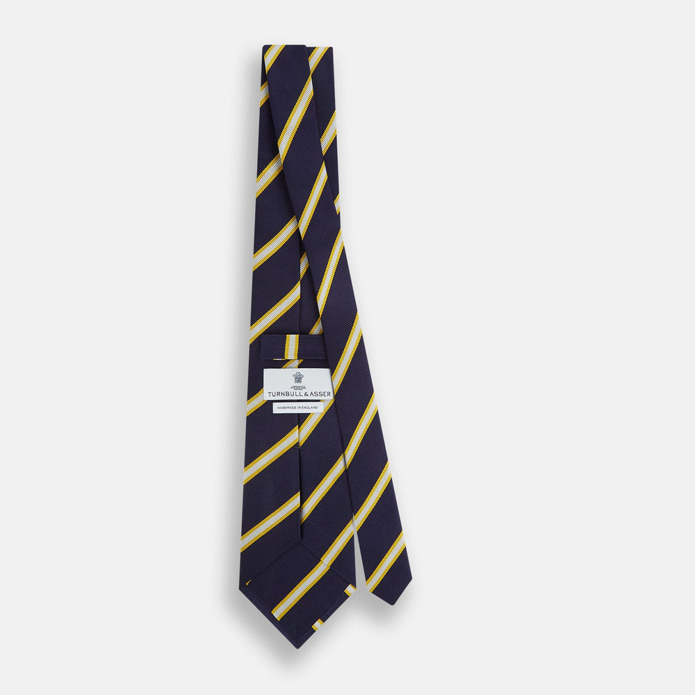 The Turnbull & Asser White and Navy Blazer Silk Tie, featuring diagonal yellow and white stripes, is rolled up neatly on a light gray background.