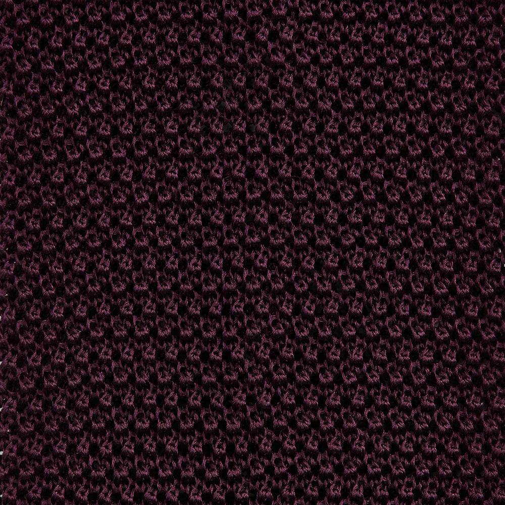 The Turnbull & Asser Knitted Burgundy Square Silk Plain Tie, featuring a textured open-weave pattern, is rolled up and displayed on a plain white background—a versatile accessory for the modern gentleman.