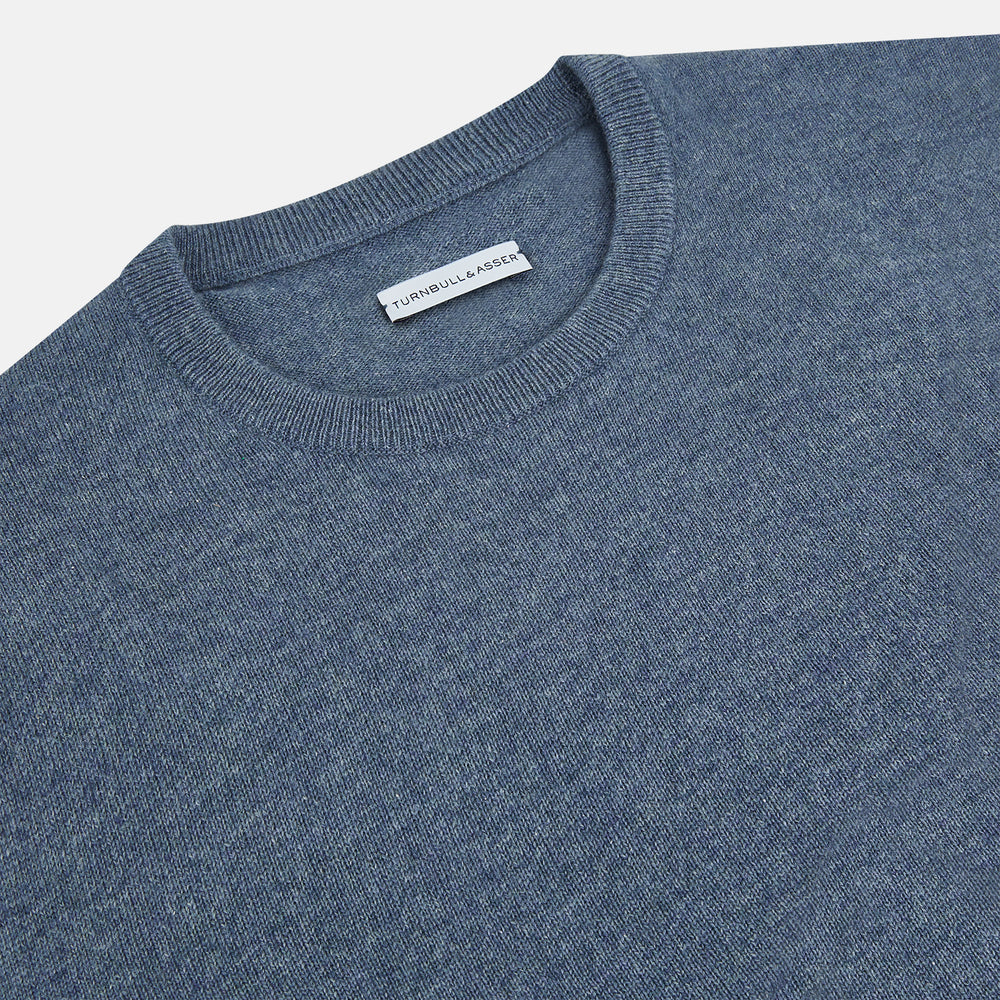 The Turnbull & Asser Pacific Blue Cashmere Round Neck Jumper features long sleeves and ribbed cuffs, hem, and neckline, shown on a light grey background.