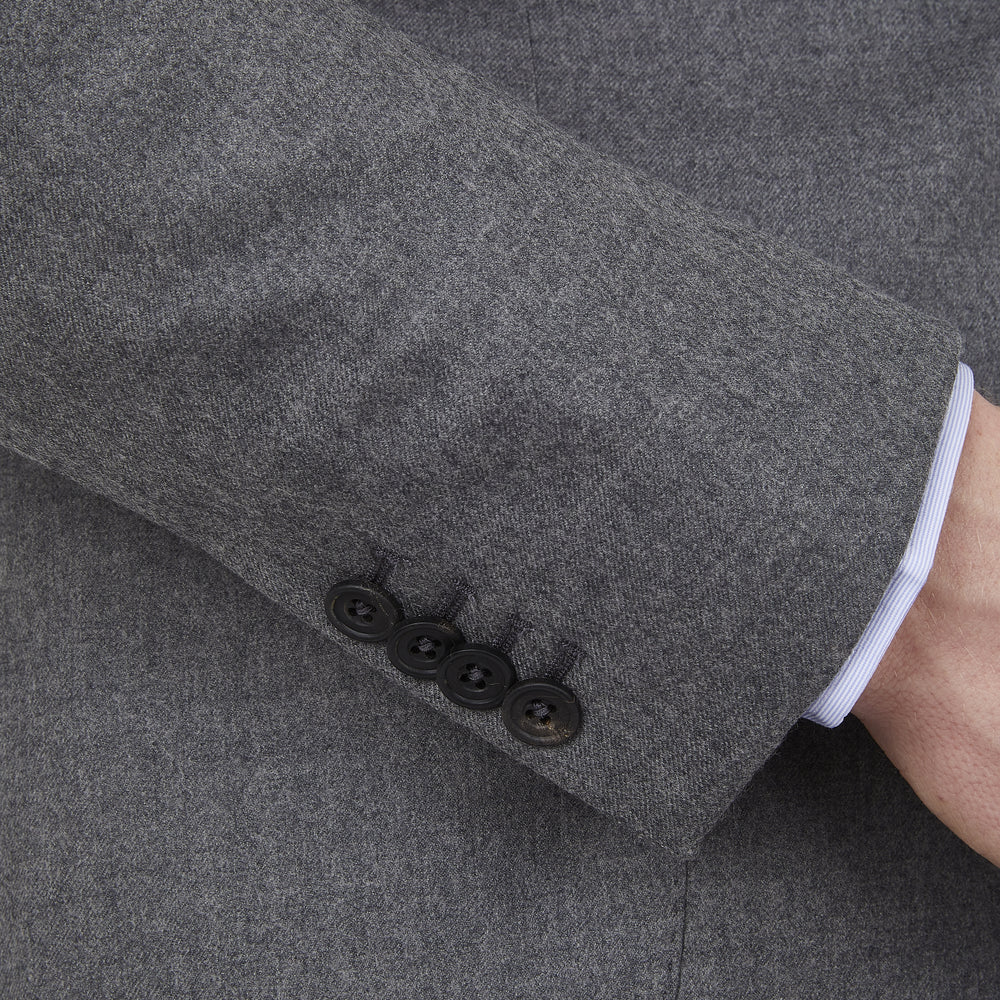 The Turnbull & Asser Grey Merino Wool Jacket is single-breasted with a notched lapel, two front patch pockets, and a single button closure, fashioned from fine Super Merino Wool. Shown here against a plain white background.