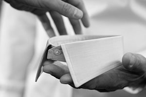 A close-up, black-and-white image showing two hands carefully holding and inspecting a detached shirt collar.