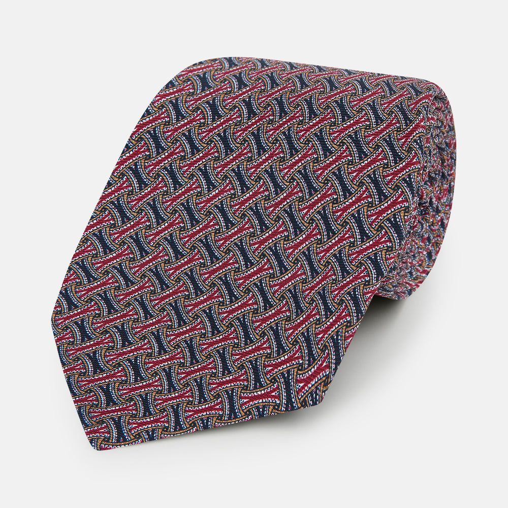The Turnbull & Asser Burgundy and Navy Weave-Patterned Printed Silk Tie features an intricate geometric design, shown rolled on a plain white background.