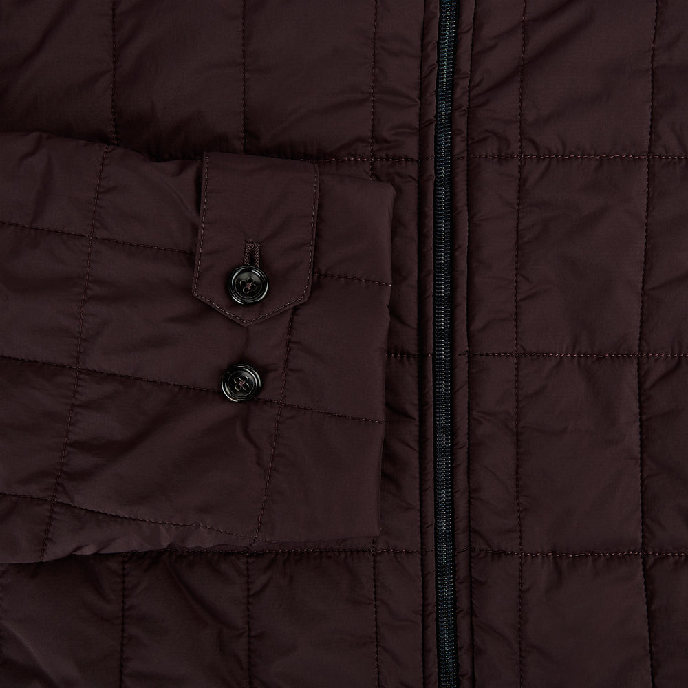 The Battersea Burgundy Quilted Jacket by Turnbull & Asser is a men's elegant outerwear featuring a front zipper, zippered side pockets, chest pocket, pointed collar, and buttoned cuffs, shown on a plain white background.