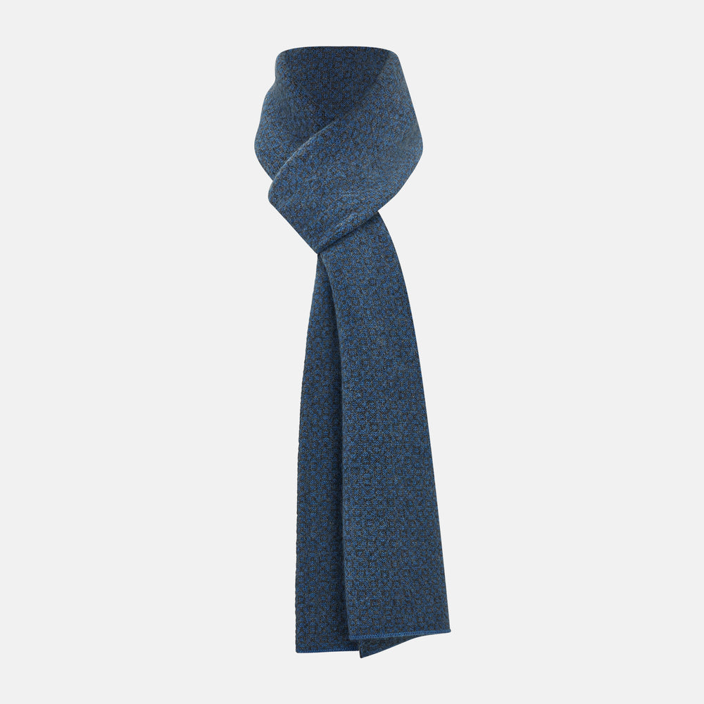The Azzurro and Graphite Lozenge-Patterned Cashmere Knitted Scarf by Turnbull & Asser features a blue geometric design and luxurious softness, displayed in a looped drape with both ends hanging against a white background.