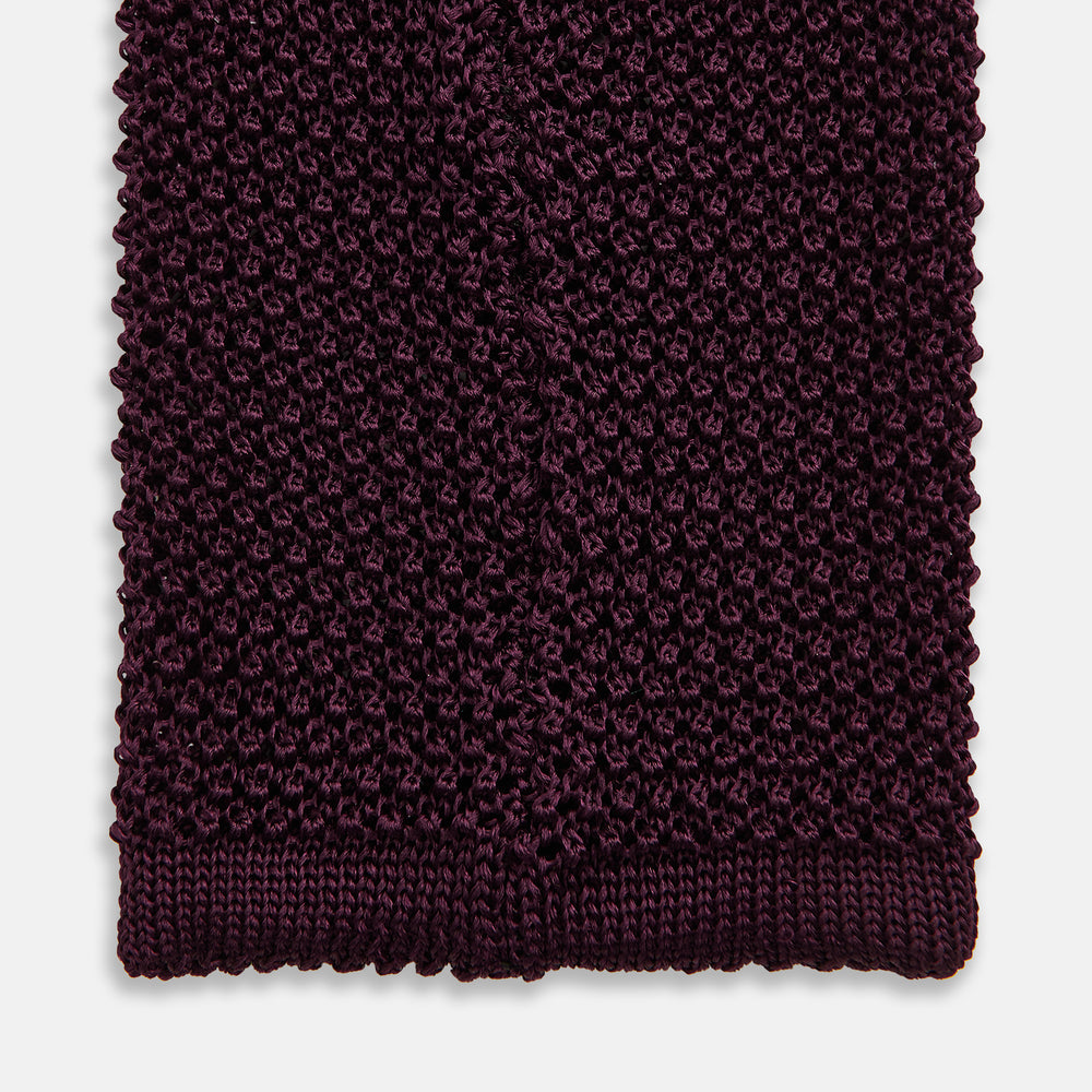 The Turnbull & Asser Knitted Burgundy Square Silk Plain Tie, featuring a textured open-weave pattern, is rolled up and displayed on a plain white background—a versatile accessory for the modern gentleman.