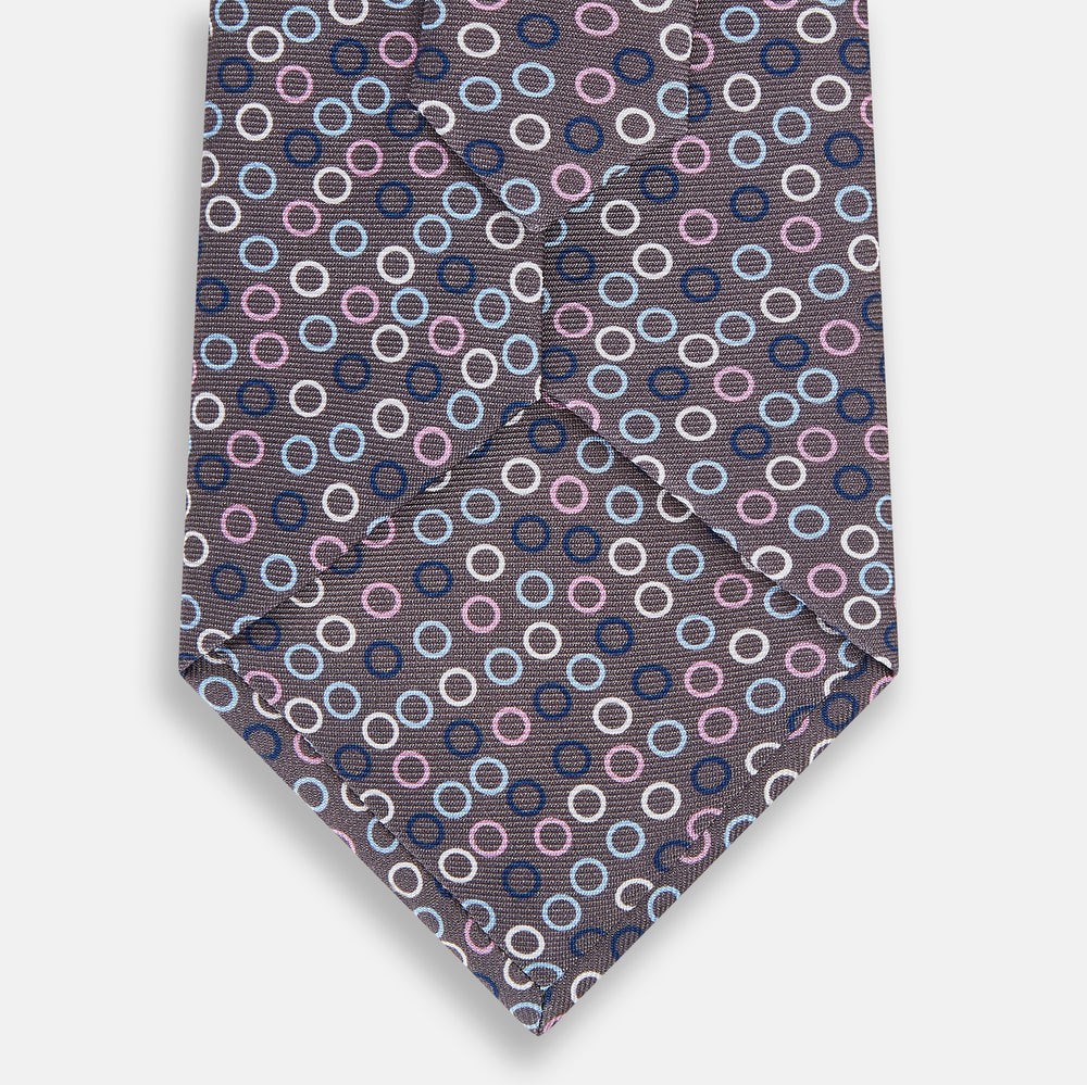 The Turnbull & Asser Purple and Blue Circle Ash Silk Tie is crafted from fine English silk and features a pattern of small blue, pink, and white circles on a dark ash background.