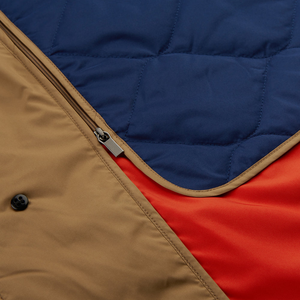 A person wears the Turnbull & Asser Camel Quintern Sealup Raincoat with Detachable Liner, paired with dark pants, standing against a plain light gray background, showing the sleek technical rainwear style with one hand in a pocket.