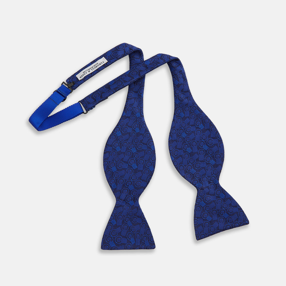 The Turnbull & Asser Electric Blue Motif Silk Bow Tie features subtle circular and swirl designs, shown on a plain white background—perfect for elevating formal attire.