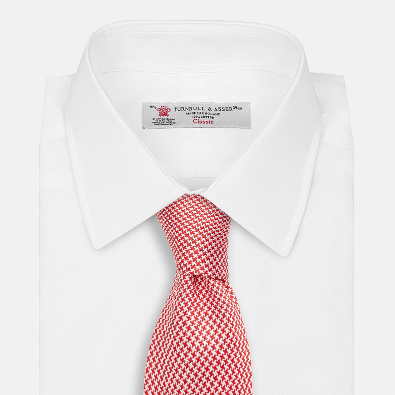 View 2 of product The Turnbull & Asser Red Houndstooth Silk Tie features a textured, small geometric pattern in red and white—ideal as a classic office accessory, shown rolled up on a plain white background.